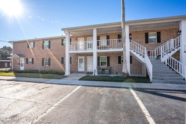 view of front of property featuring stairs, uncovered parking, and brick siding