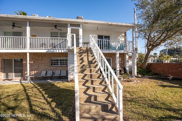 rear view of house with a yard, stairway, a ceiling fan, and brick siding