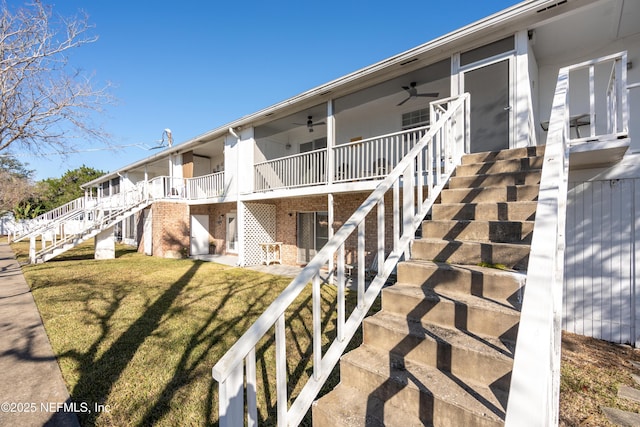 view of side of property featuring a yard, brick siding, ceiling fan, and stairs