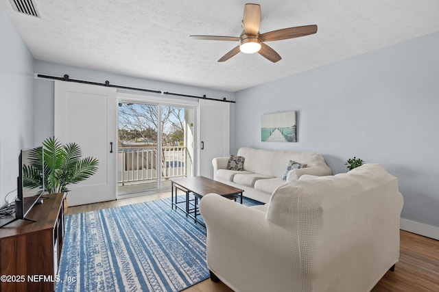 living room featuring wood finished floors, visible vents, a textured ceiling, and a barn door