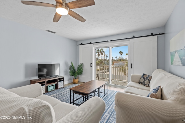 living room with visible vents, a barn door, a ceiling fan, a textured ceiling, and wood finished floors