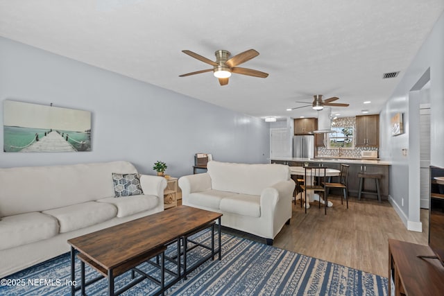 living room with baseboards, visible vents, ceiling fan, and wood finished floors