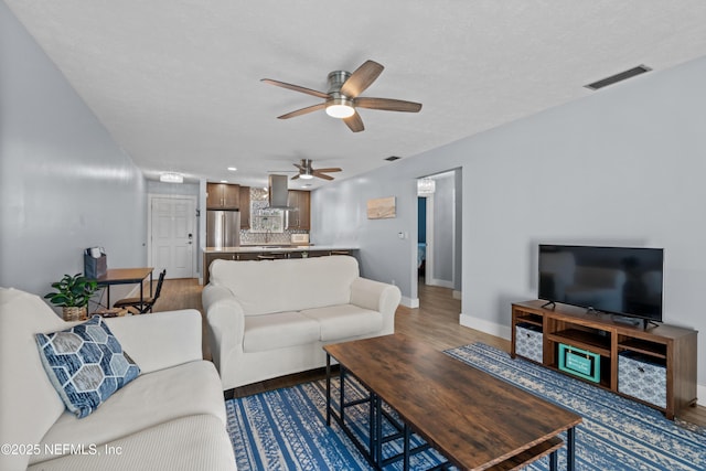 living area featuring visible vents, a textured ceiling, baseboards, and wood finished floors