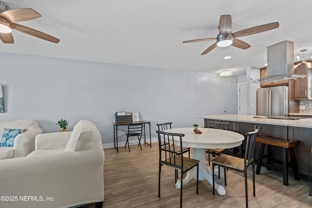 dining space with a ceiling fan, light wood-style flooring, and baseboards