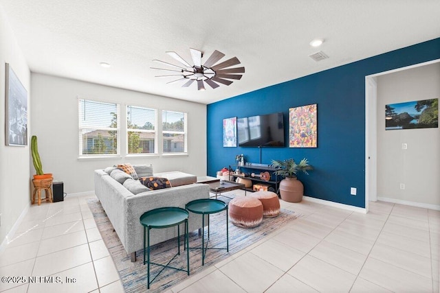 living area with tile patterned flooring, a ceiling fan, visible vents, and baseboards