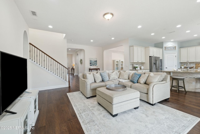 living room with dark wood-style floors, arched walkways, recessed lighting, visible vents, and stairs