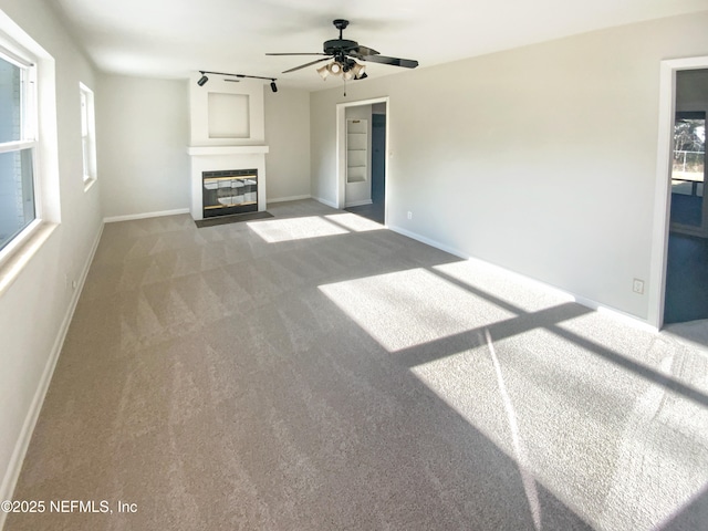 unfurnished living room featuring baseboards, a fireplace with flush hearth, ceiling fan, rail lighting, and carpet