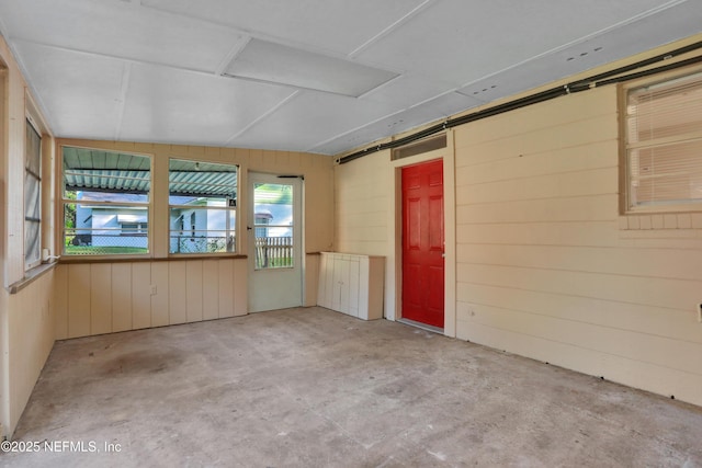 spare room featuring a barn door, wood walls, and unfinished concrete floors