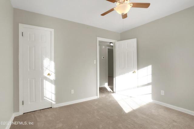 empty room featuring a ceiling fan, light colored carpet, and baseboards