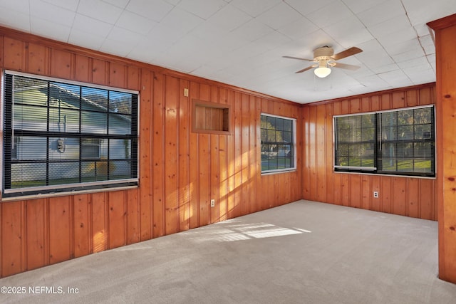 spare room with ceiling fan, wooden walls, ornamental molding, and light colored carpet