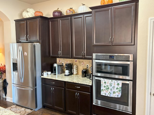 kitchen with dark brown cabinets, stainless steel appliances, dark wood-type flooring, and light stone counters