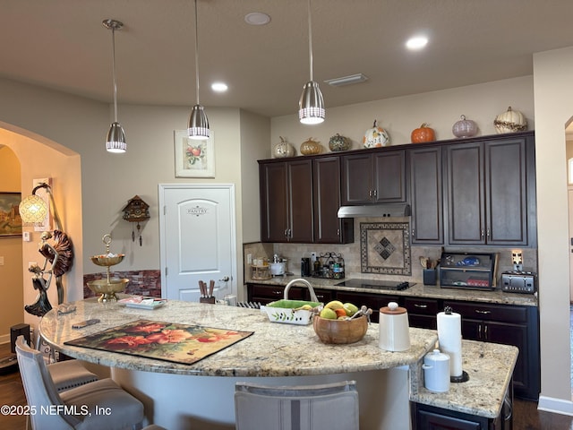 kitchen with a center island with sink, hanging light fixtures, dark brown cabinets, a breakfast bar area, and decorative backsplash