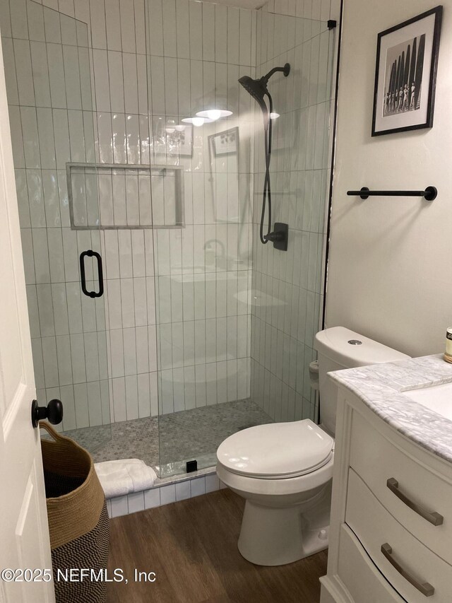 bathroom featuring vanity, wood finished floors, toilet, and a shower stall