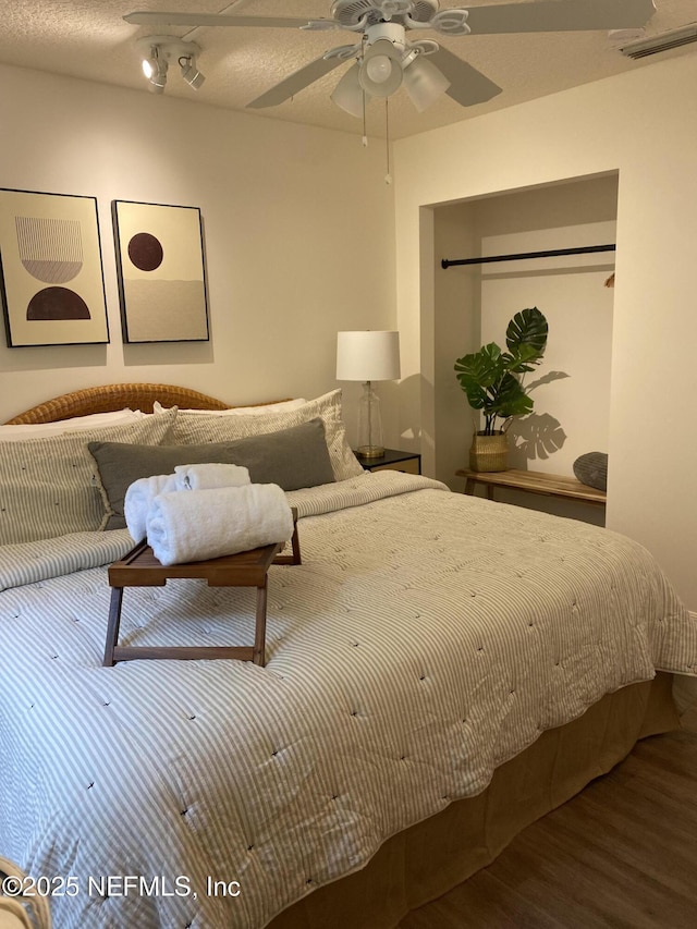 bedroom with a ceiling fan, visible vents, a textured ceiling, and wood finished floors