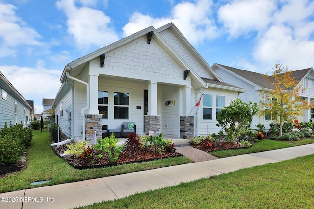 craftsman house featuring stone siding, a front yard, and covered porch