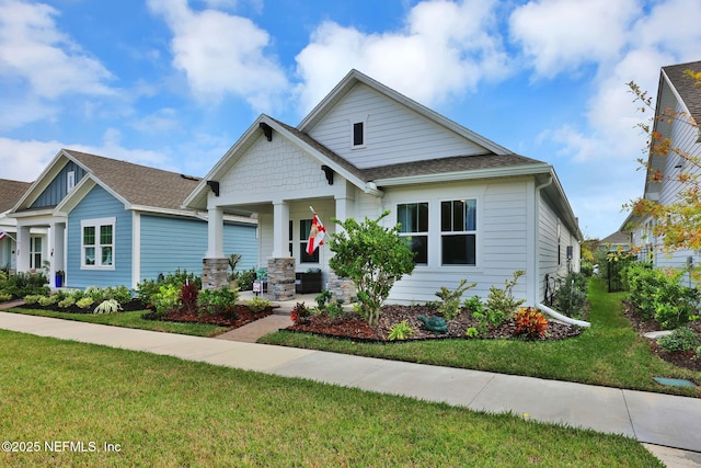 view of front of property featuring covered porch, a shingled roof, a front yard, and cooling unit