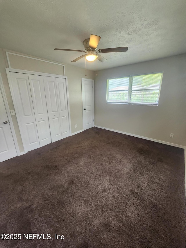 unfurnished bedroom with a textured ceiling, ceiling fan, baseboards, a closet, and dark carpet