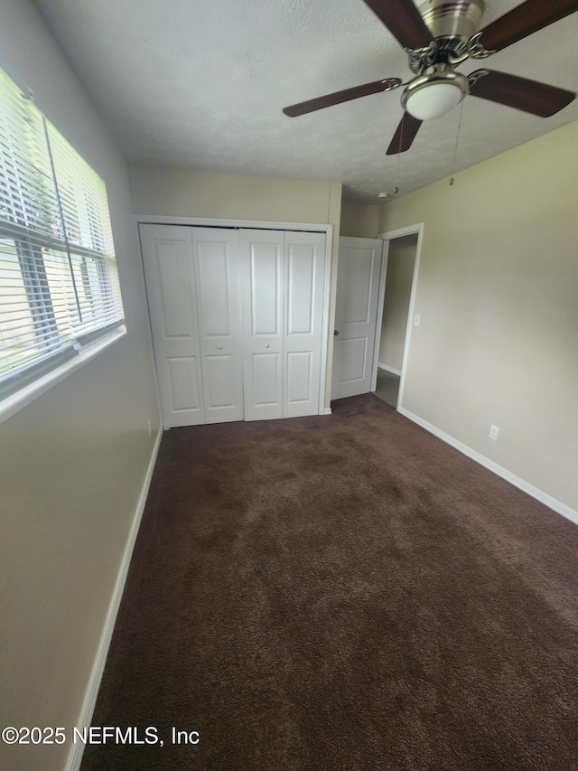 unfurnished bedroom featuring a ceiling fan, baseboards, dark carpet, and a closet