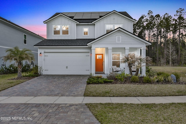 view of front facade with a porch, a garage, decorative driveway, roof mounted solar panels, and board and batten siding