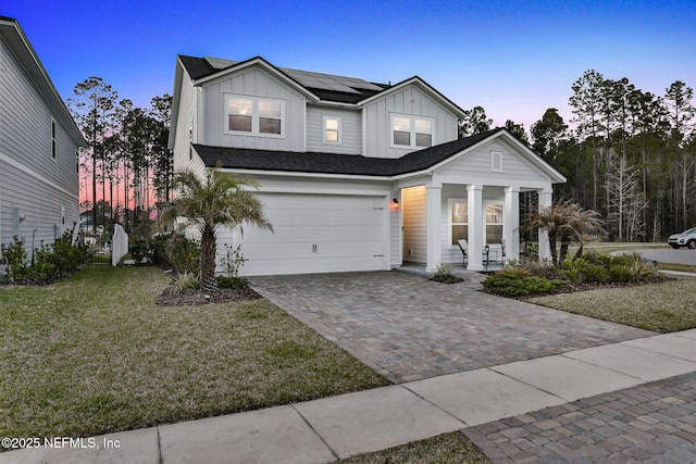 view of front of home with a garage, solar panels, decorative driveway, a yard, and board and batten siding