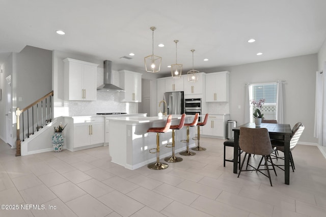 kitchen featuring a center island with sink, stainless steel fridge with ice dispenser, light countertops, wall chimney range hood, and a kitchen bar