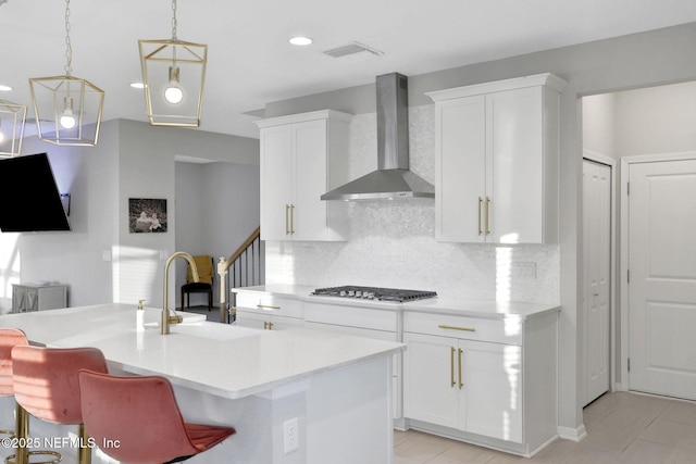 kitchen featuring gas cooktop, a sink, light countertops, wall chimney exhaust hood, and tasteful backsplash