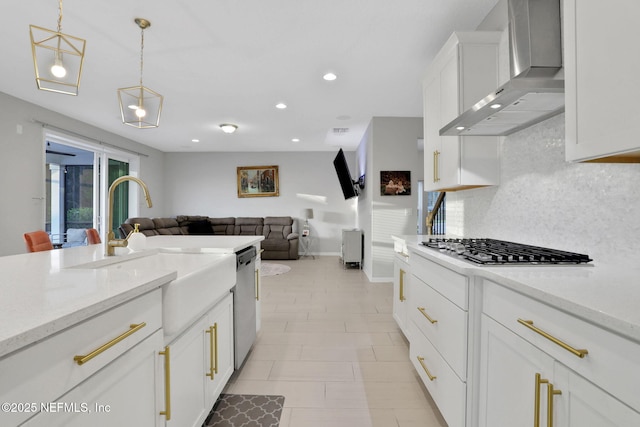 kitchen featuring a sink, white cabinetry, wall chimney range hood, appliances with stainless steel finishes, and tasteful backsplash