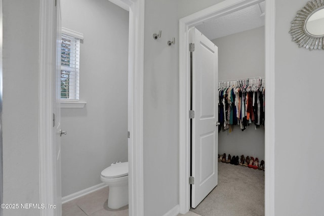 bathroom featuring a spacious closet, toilet, a textured ceiling, baseboards, and tile patterned floors