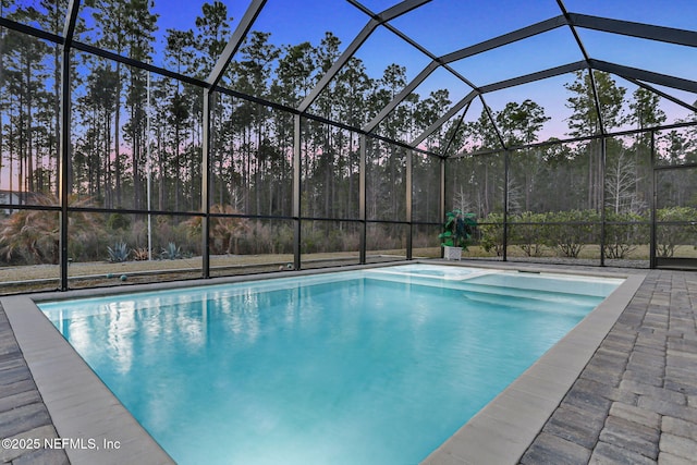 pool at dusk with glass enclosure, an outdoor pool, and a patio