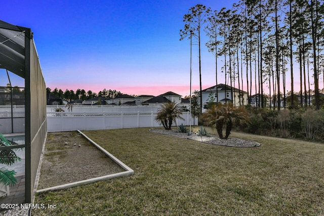 yard at dusk featuring a lanai and fence