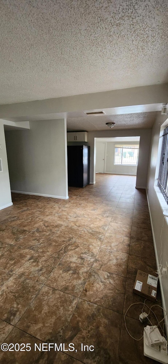 spare room featuring a textured ceiling, visible vents, and baseboards