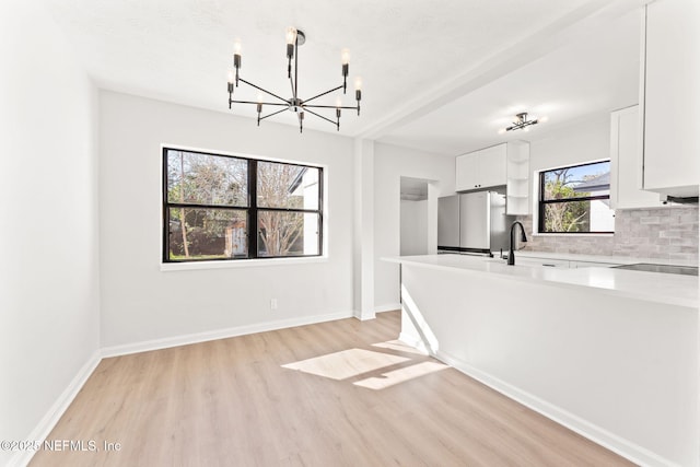 kitchen with light countertops, backsplash, light wood-style floors, freestanding refrigerator, and white cabinetry