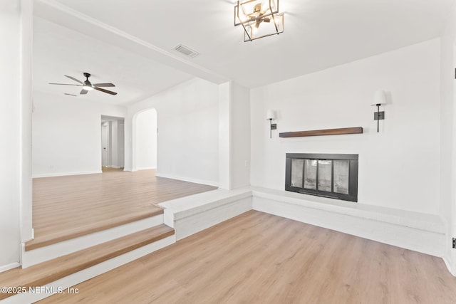 spare room featuring arched walkways, visible vents, a glass covered fireplace, wood finished floors, and baseboards