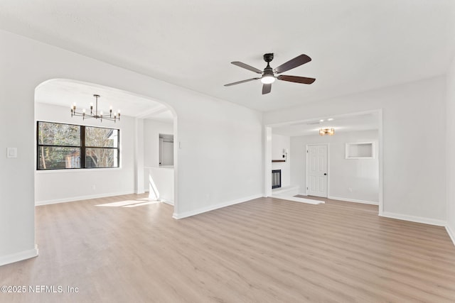 unfurnished living room with arched walkways, light wood-style flooring, a glass covered fireplace, baseboards, and ceiling fan with notable chandelier