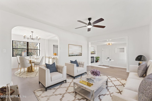 living room with arched walkways, baseboards, and ceiling fan with notable chandelier