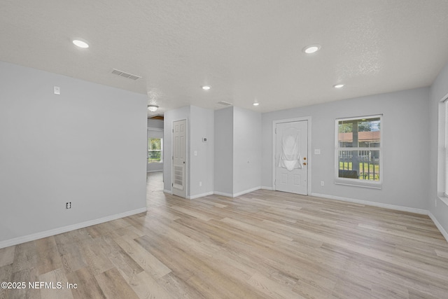 empty room with light wood-type flooring and a textured ceiling