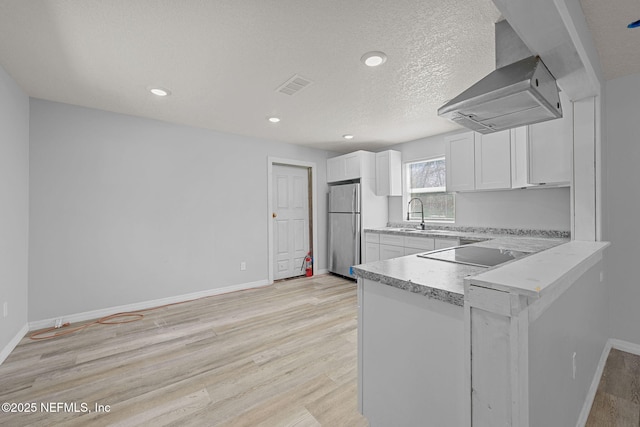 kitchen featuring island exhaust hood, black electric cooktop, light hardwood / wood-style floors, stainless steel fridge, and white cabinetry