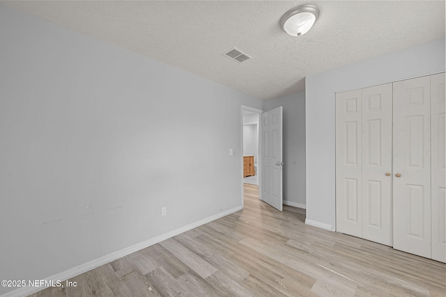 unfurnished bedroom featuring light wood-type flooring, a closet, and a textured ceiling