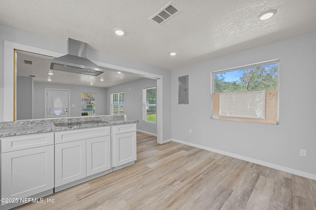 kitchen with light stone counters, white cabinets, island exhaust hood, black electric cooktop, and light hardwood / wood-style floors