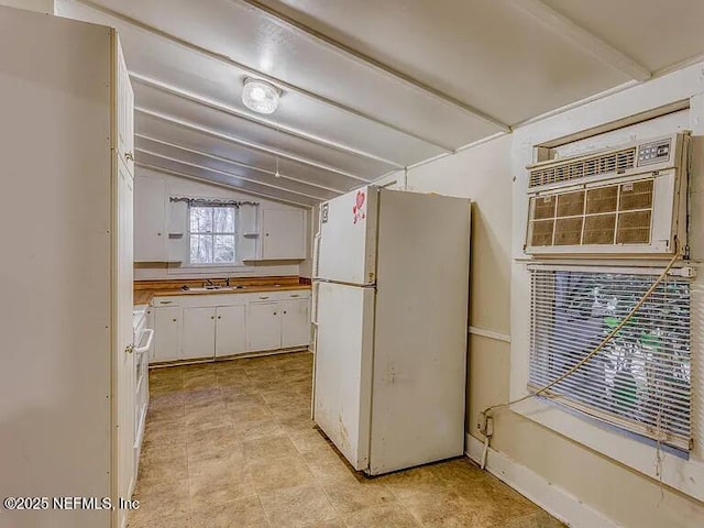 kitchen with stove, freestanding refrigerator, vaulted ceiling, white cabinetry, and a sink