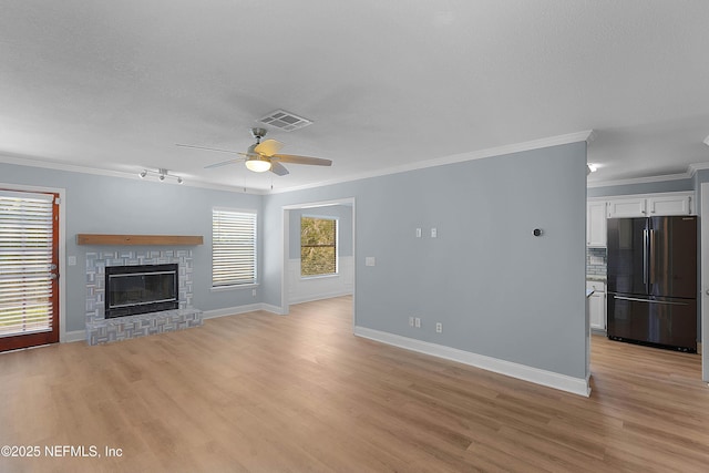 unfurnished living room featuring light wood finished floors, visible vents, a brick fireplace, and crown molding