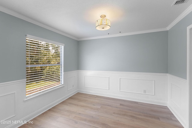 unfurnished room with visible vents, wainscoting, crown molding, and light wood-type flooring