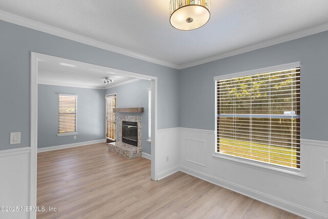 unfurnished living room with crown molding, wainscoting, a fireplace, and light wood finished floors