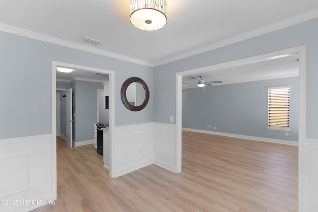 unfurnished room with light wood-type flooring, visible vents, wainscoting, crown molding, and ceiling fan