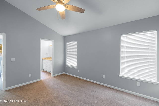 unfurnished bedroom with a ceiling fan, ensuite bathroom, baseboards, light colored carpet, and vaulted ceiling