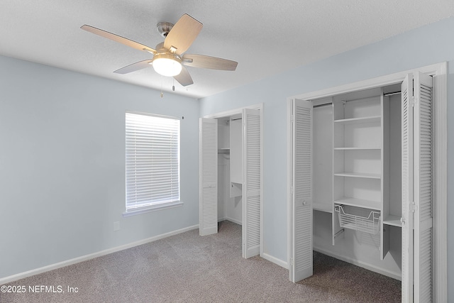 unfurnished bedroom featuring carpet, baseboards, ceiling fan, multiple closets, and a textured ceiling