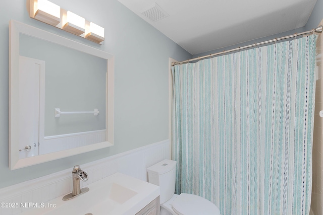 full bathroom with visible vents, curtained shower, toilet, wainscoting, and vanity