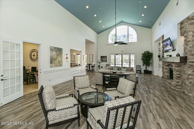 living room with hardwood / wood-style flooring, ceiling fan, a stone fireplace, and high vaulted ceiling