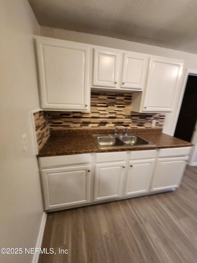 kitchen with tasteful backsplash, dark countertops, white cabinetry, a sink, and wood finished floors