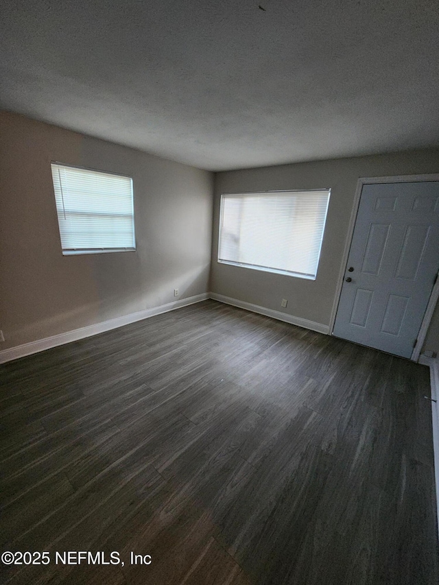 unfurnished bedroom with a textured ceiling, baseboards, and dark wood-style flooring